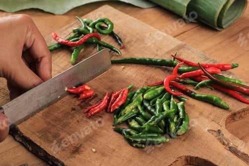 Preview: Female Hand Slicing Cut Chilli Pepper on Wooden Chopping Board Using Knife