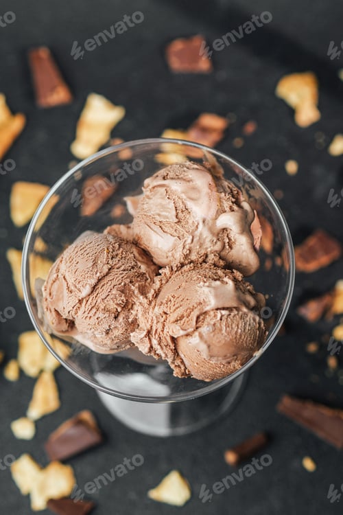 Preview: Closeup of chocolate ice cream scoops in glass with waffle crumbs on dark surface