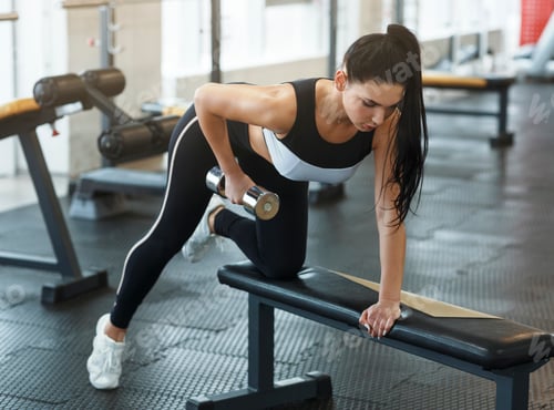 Preview: Pretty young woman with dumbbell doing push ups in gym