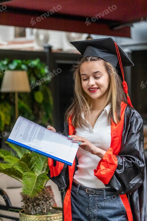 Preview: Beautiful lady wearing graduation cape and looking at her notebook