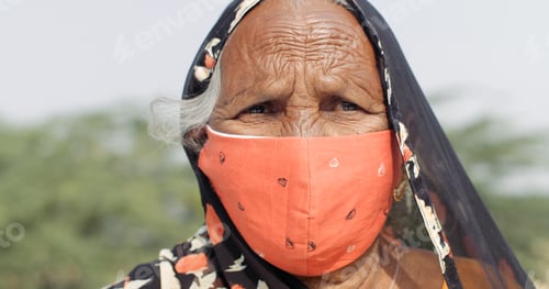 Preview: Closeup of an elderly South Asian woman wearing a headscarf and a bright orange Coronavirus mask
