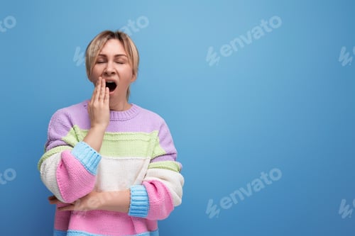 Preview: portrait of tired blond woman in casual outfit yawning on blue background with copy space