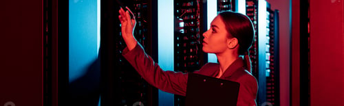 Preview: panoramic shot of businesswoman holding clipboard and looking at server room