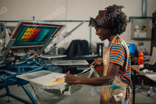 Preview: Interracial printing shop worker taking product off screen printing press