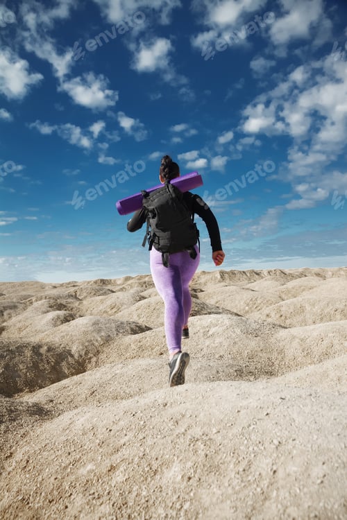 Preview: woman solo tourist running in jump, rear view on hill area in sportswear backpack, healthy lifestyle