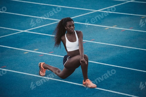Preview: A black athlete of African origin performs stretching exercises on a blue athletics track.