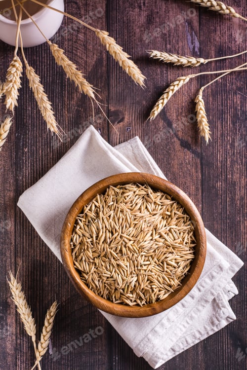 Preview: A plate with unpeeled oat seeds and ears of oats on a wooden table. Top and vertical view
