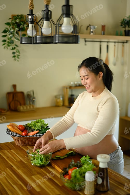 Preview: Expecting mother preparing a salad with fresh vegetables in home kitchen