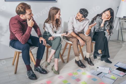 Preview: happy multicultural coworkers sitting on chairs in office