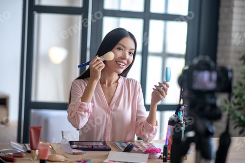 Preview: Blogger holding brush while filming makeup tutorial