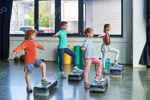 Preview: four pretty children in sportswear exercising with fitness steppers with arms aside, child sport