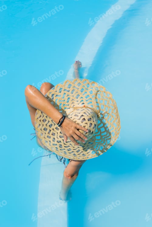 Preview: Pretty woman in a hat enjoying a swimming pool