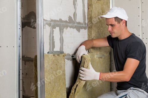 Preview: Worker in protective gloves insulating rock wool insulation in wooden frame
