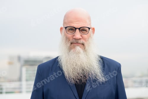 Preview: Face of mature bald bearded businessman with eyeglasses against view of the city