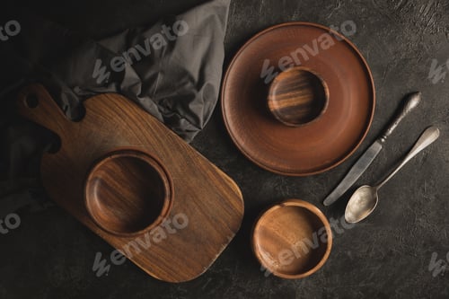 Preview: flat lay with wooden cutting board, plates, bowls and rustic silverware isolated on black tabletop