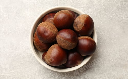 Preview: Roasted edible sweet chestnuts in bowl on light grey table, top view