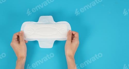 Preview: Hand is hold a sanitary napkin with wings top view on blue background.