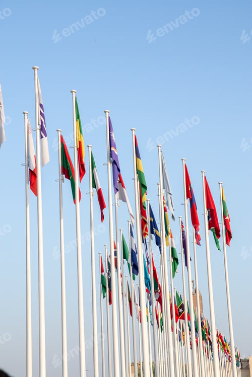 Preview: Vertical shot of tall poles with world countries flags against a clear sky