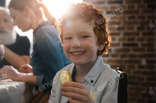 Visualização: foco seletivo de menino sorridente com pedaço de pepino olhando para a câmera