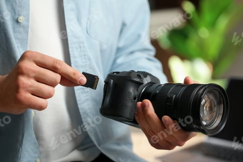 Preview: Man inserting SD memory card into photo camera indoors, closeup