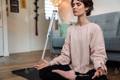 Preview: Peaceful beautiful girl meditating while sitting on mat at home