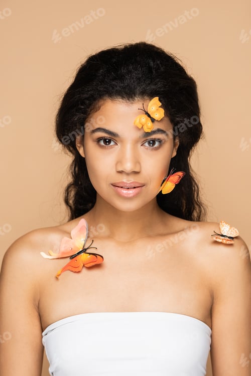 Preview: pretty african american woman with orange butterflies on face and bare shoulders looking at camera