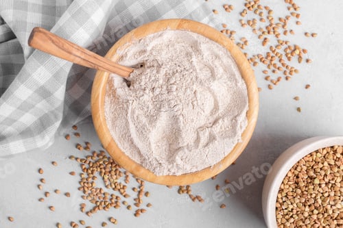 Preview: Buckwheat flour in a wooden bowl with spoon and raw green buckwheat grain on grey background