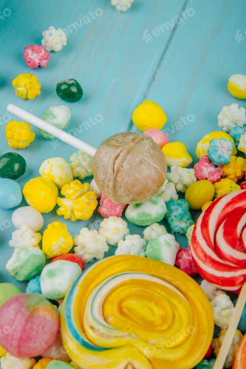Preview: side view of lollipop candies and colorful candies scattered on blue background