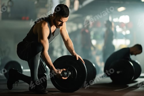 Preview: Young sportsman adjusting barbell on weight training in a gym.