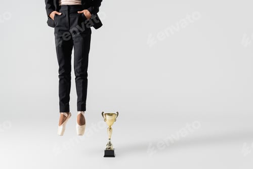 Preview: cropped view of african american businesswoman in pointe shoes jumping near golden cup on grey