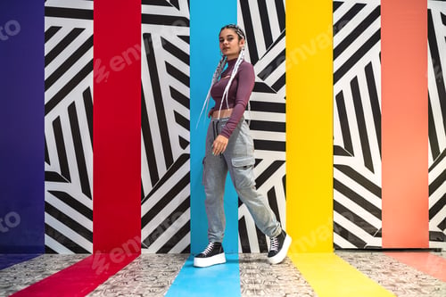 Preview: Young woman standing looking at camera against wall with colors and striped designs