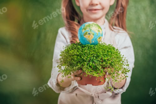 Preview: selective focus of kid holding flower pot with plant and globe model on blurred background, earth