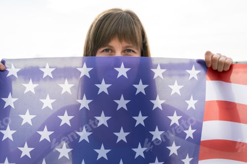 Preview: Portrait of happy smiling girl hiding her face behind USA national flag.