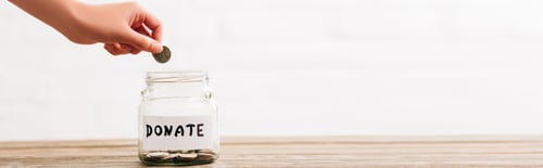 Preview: cropped view of woman putting coin in penny jar with donate lettering on wooden surface on white