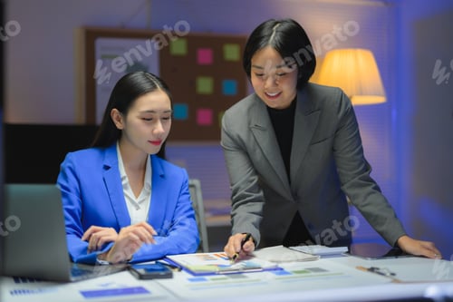 Preview: Two Young Businesswomen Working Late Analyzing Charts in Office at Night