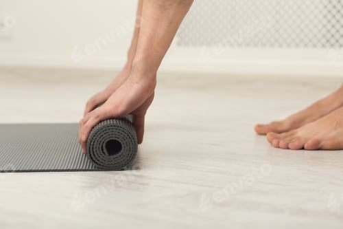 Preview: Hands rolling up a gray yoga mat on floor