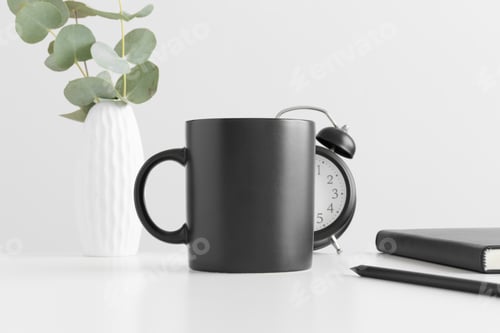Preview: Black mug mockup with eucalyptus in a vase and workspace accessories on a white table.