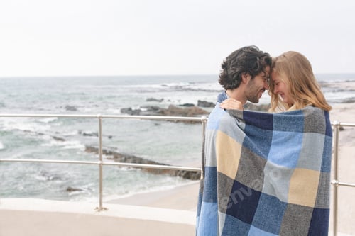 Preview: Couple wrapped in blanket standing at promenade near beach om a sunny day