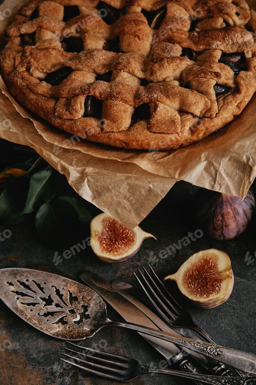 Preview: close up view of homemade pie on baking paper, antique cutlery and fresh figs on dark tabletop