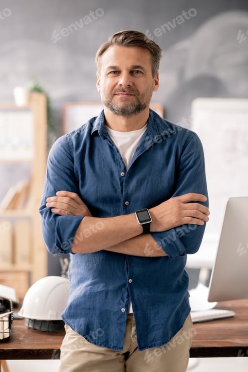 Preview: Bearded smiling engineer with arms crossed on chest standing in front of camera