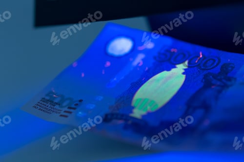 Preview: Currency under UV light reveals security features in a dark setting