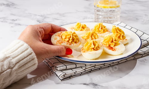Preview: stuffed eggs with paprika, on a plate, a woman's hand reaches for it,