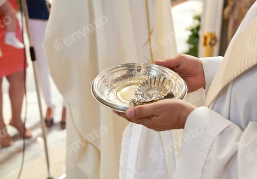 Preview: Priest holding a silver bowl with holy water for a baptism ceremony in a church