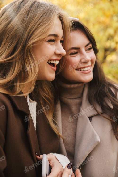 Preview: Two cheerful young pretty girls wearing coats walking together