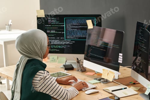 Preview: Young woman in hijab typing on computer keyboard while decoding data