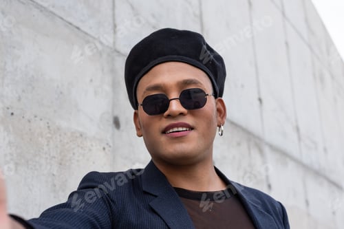 Vista previa: Joven latino gay maquillado con un sombrero de moda y gafas de sol