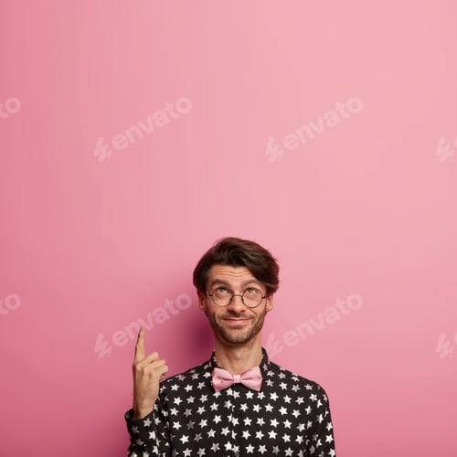 Preview: Vertical image of glad hipster with stubble points index finger above, dressed in fashionable elegan