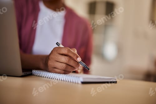 Preview: A close-up of an unknown female writing notes in a notebook at the wooden table.