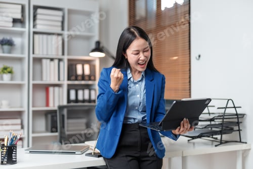 Preview: Businesswoman celebrating success holding tablet in modern office
