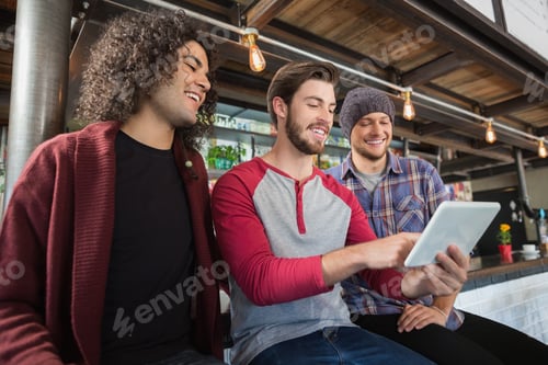 Preview: Happy male friends using digital tablet in restaurant